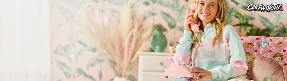 Young woman outside wearing a pink Daisy Duck sweater in honor of Daisy Duck's 85th birthday. Text: Cakeworthy.