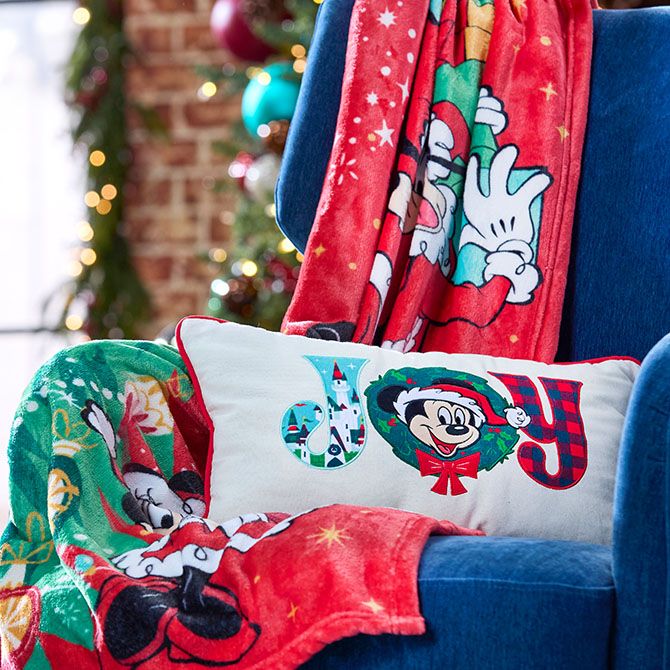 Blue chair with a Disney holiday blanket and a pillow that spells "JOY" with Mickey Mouse's face, in a festively decorated living room.