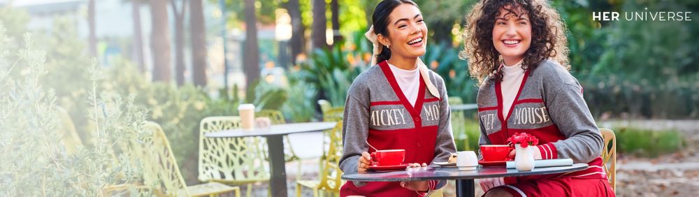 Two people wear red plaid shirts with Minnie Mouse holiday embroidery. Gift boxes and a decorated Christmas tree are in the background.