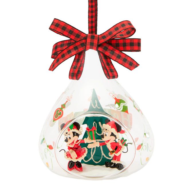 Glass ornament with Minnie and Mickey Mouse in Santa outfits, exchanging gifts in front of a Christmas tree, topped with a red plaid bow.