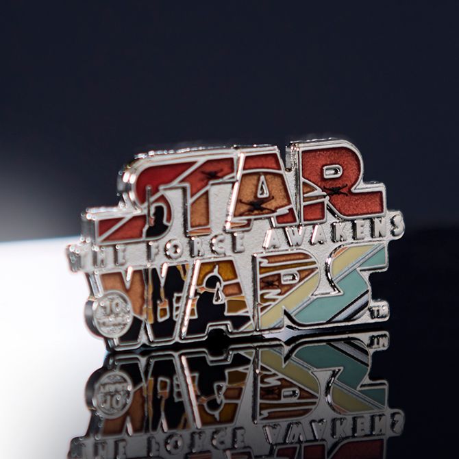Star Wars: The Force Awakens logo pin with metallic finish and retro colors, displayed on a glossy reflective surface.