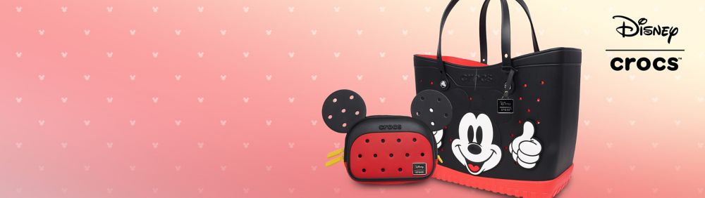 Disney x Crocs blue shoes featuring Mickey Mouse and friends with colorful designs and star-shaped Jibbitz charms on a pink background.