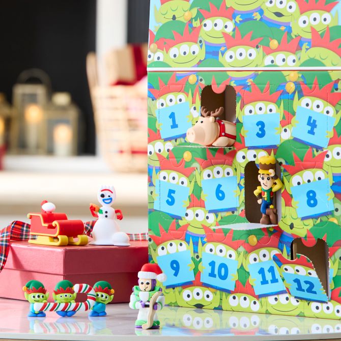 Colorful Toy Story advent calendar with small character figures, numbered doors, and festive decorations. Background includes gift boxes and lanterns.