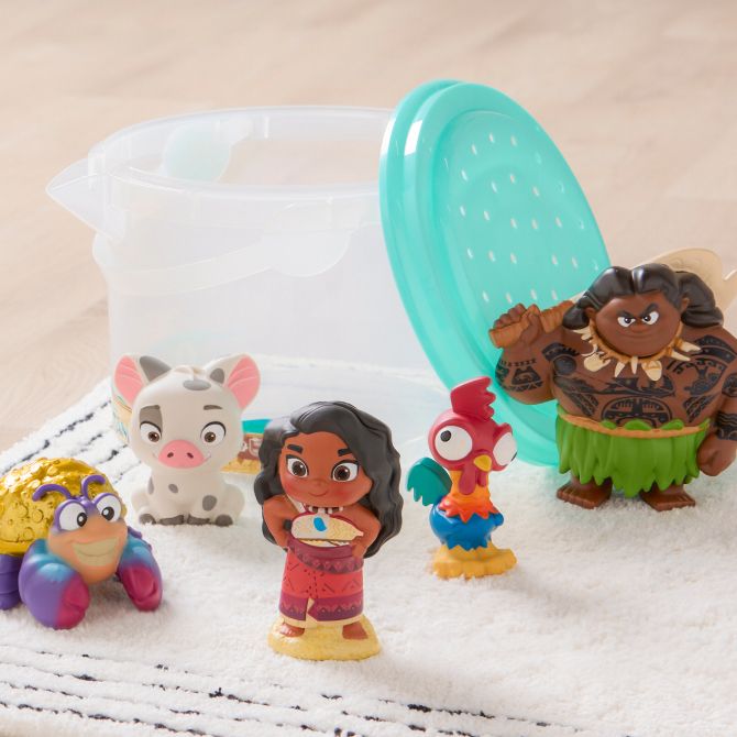 Moana, Maui, Pua, Hei Hei, and Tamatoa figures are set on a white rug with a clear play bucket and teal lid, against a light wood floor.