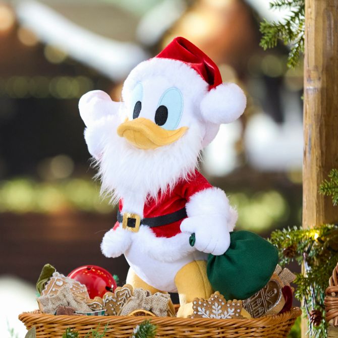 Donald Duck plush dressed as Santa with a white beard and red hat stands in a festive basket, surrounded by greenery and holiday decorations.