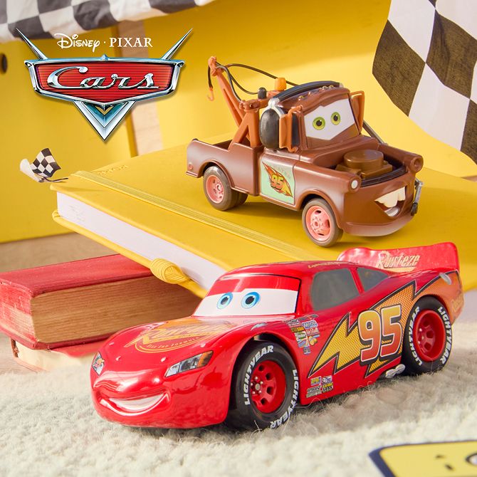Toy cars of Mater and Lightning McQueen sit on yellow books, with black-and-white checkered flags and the Disney Pixar Cars logo in the background.