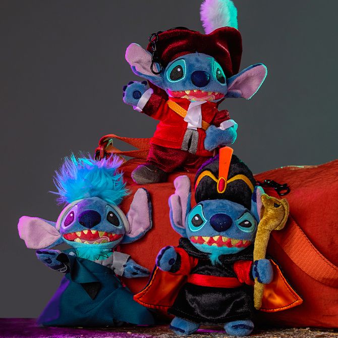 Four Stitch plush toys dressed as Captain Hook, Hades, Jafar, and Oogie Boogie are arranged on a rustic table with an orange bag and dark background.