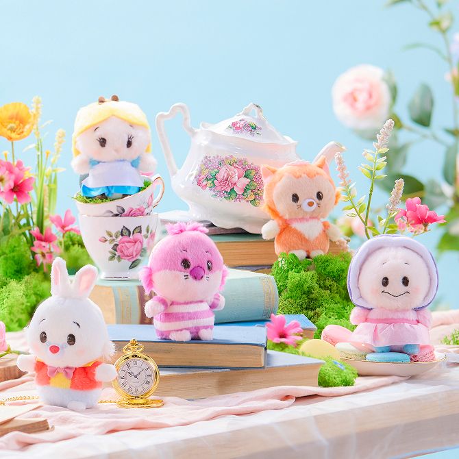 Five Alice in Wonderland plushies, a teapot, cups, books, and flowers are arranged on a pastel tea party table with a blue background.