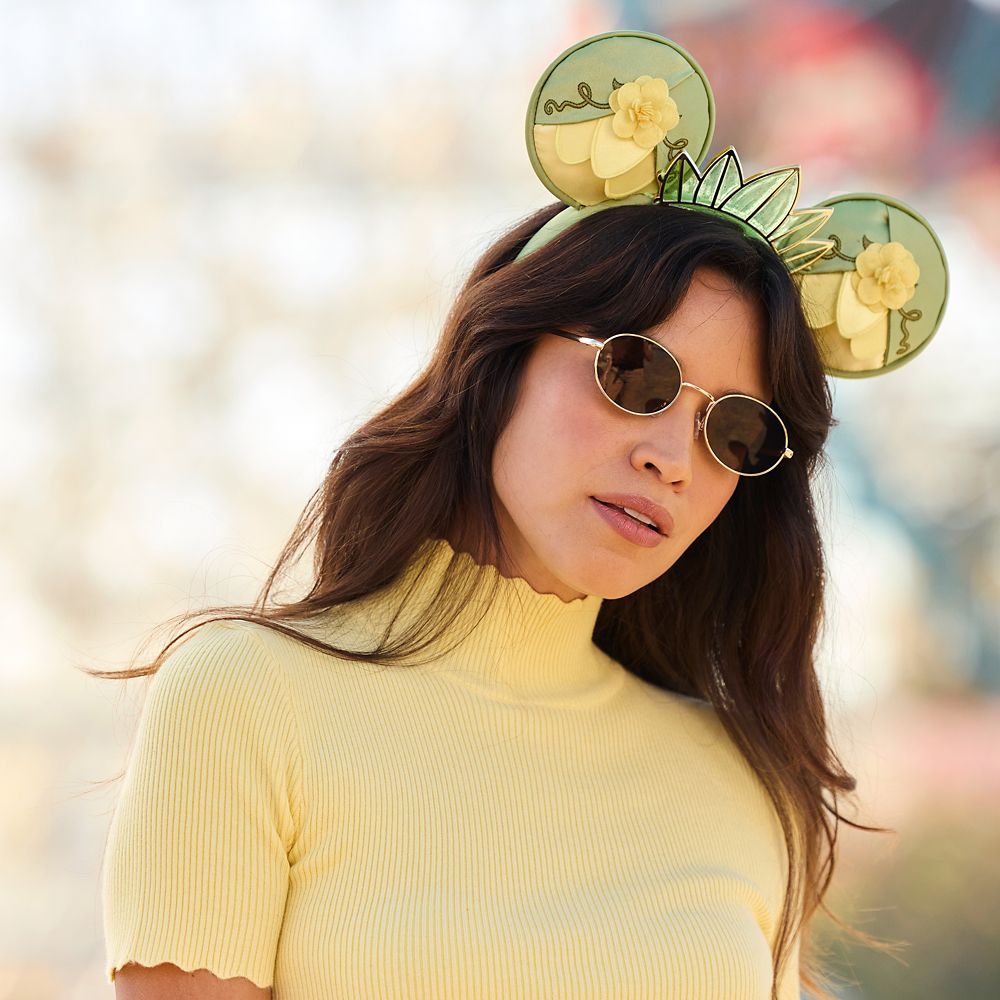 Person wearing light blue Minnie Mouse ears with a glittery bow, paired with a cozy white sweater, against a purple background.