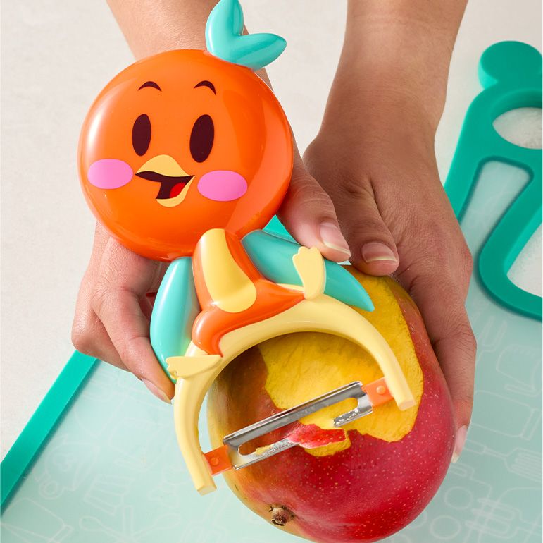 Orange bird fruit peeler against a teal cutting board.
