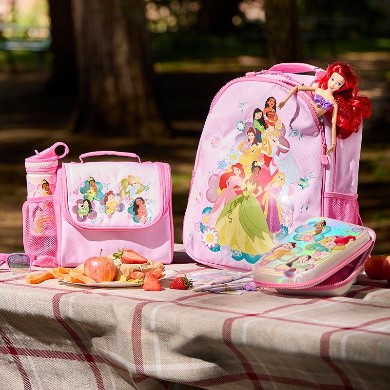 Pink Disney Princess backpack, lunchbox, and water bottle set on a picnic table with snacks. Ariel doll seen sticking out of backpack.